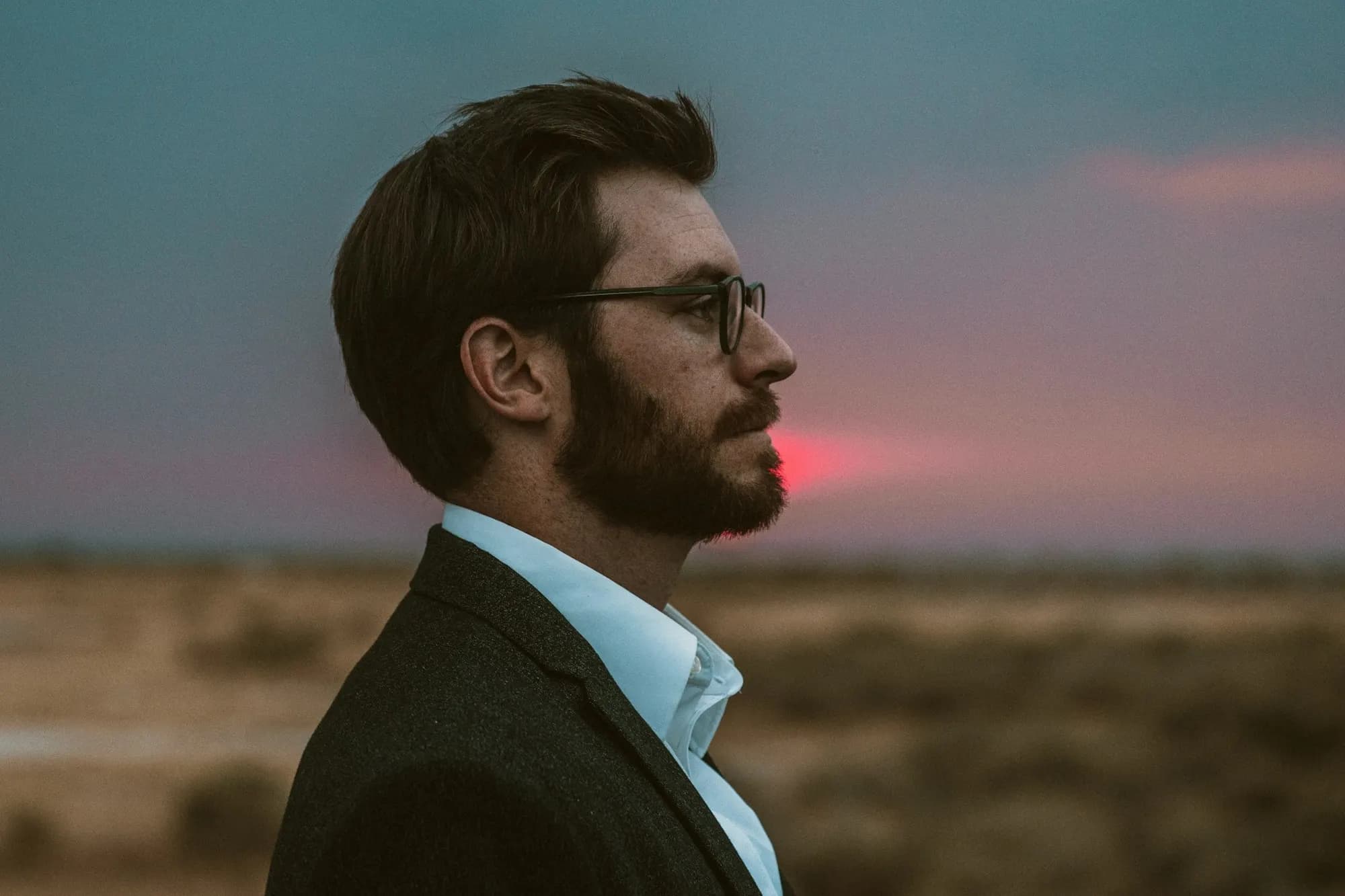 hombre de saco y anteojos de perfil al atardecer