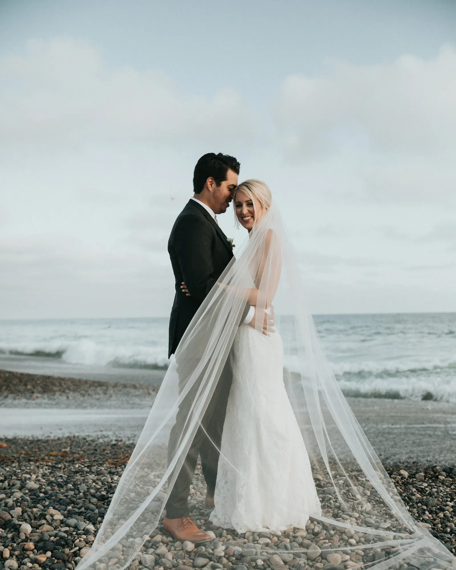 novios abrazados en la playa, con el velo largo al viento
