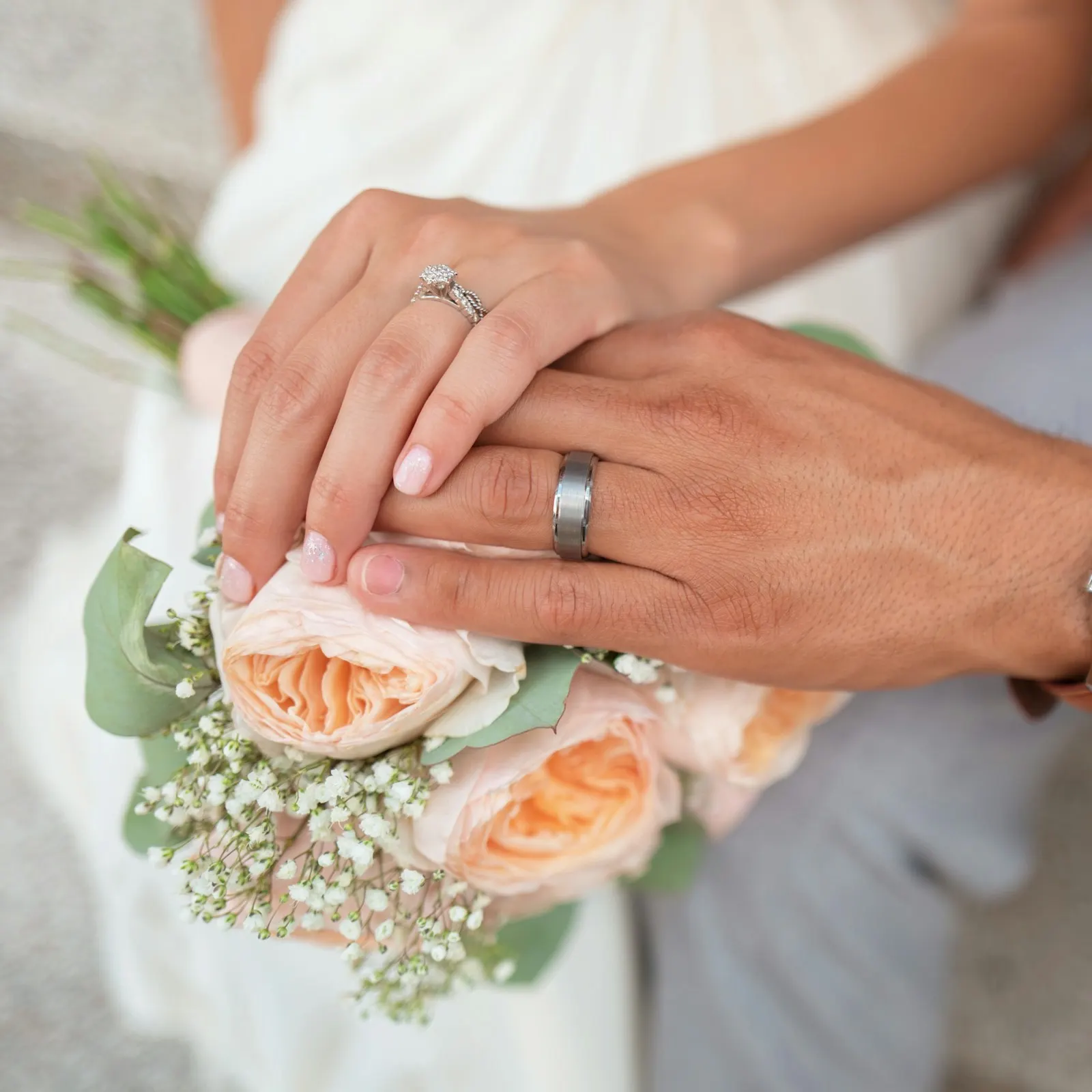 manos de los novios con anillos sobre el ramo