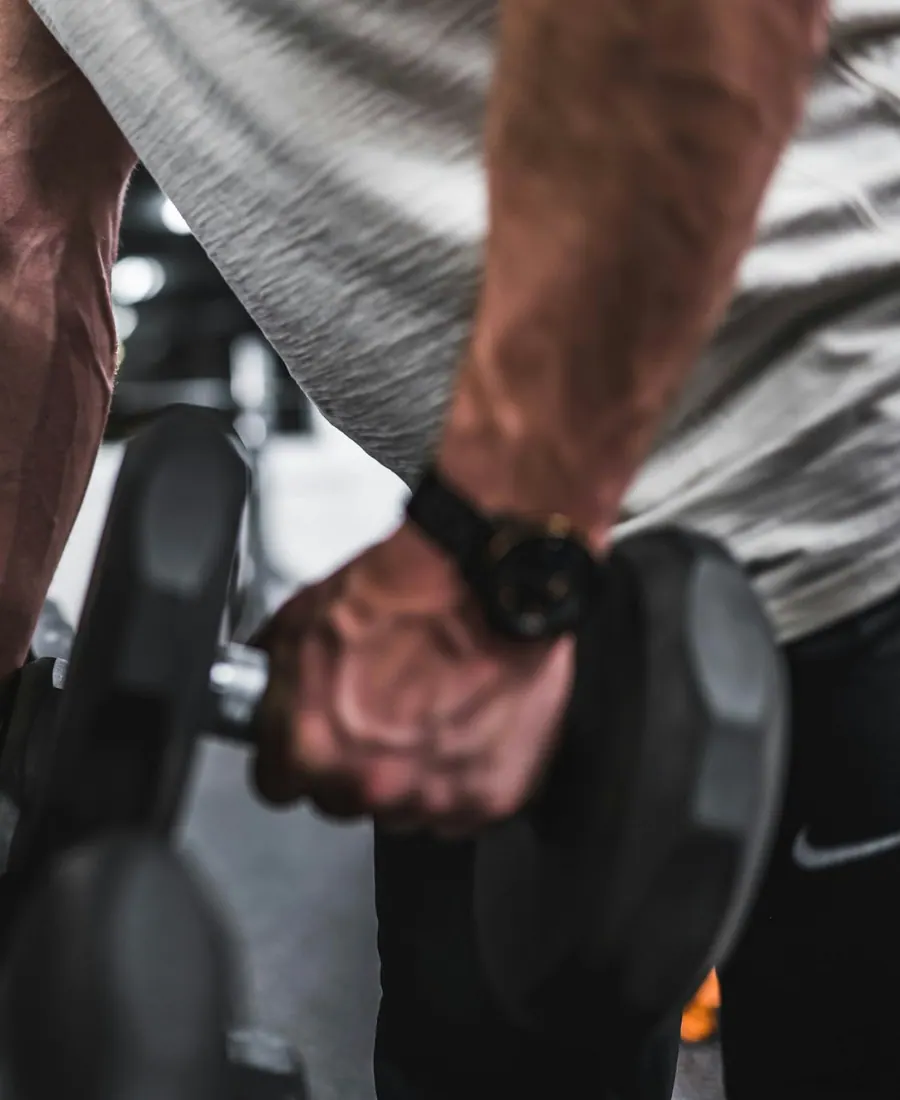 Mano con reloj agarrando una mancuerna en un gimnasio en penumbra