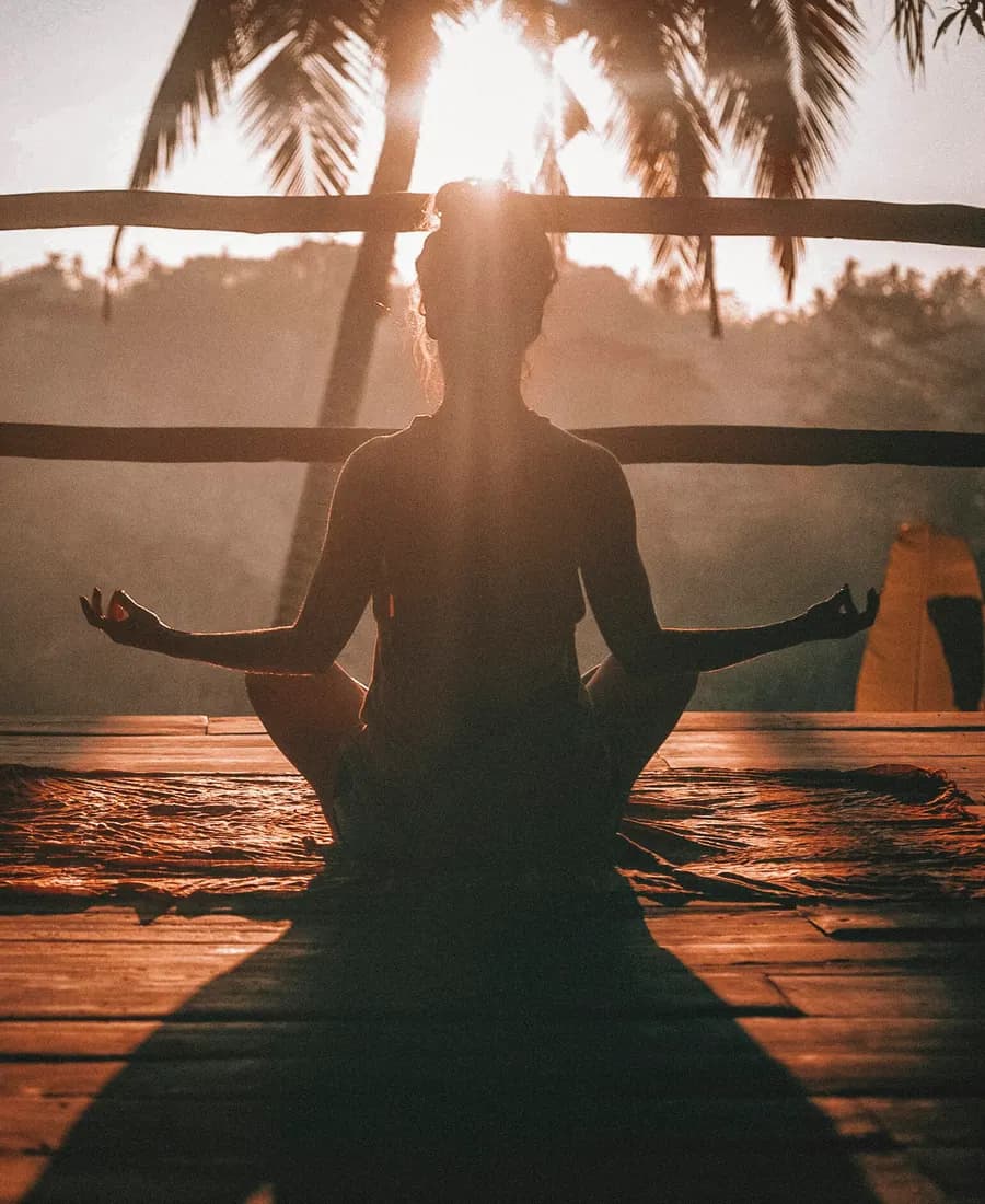 Silueta de una persona sentada en postura de yoga frente a una ventana al atardecer