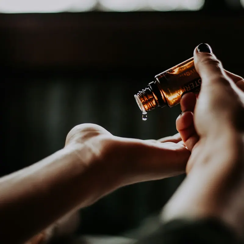 Manos aplicando unas gotas de sérum con un frasco gotero ámbar, con luz cálida