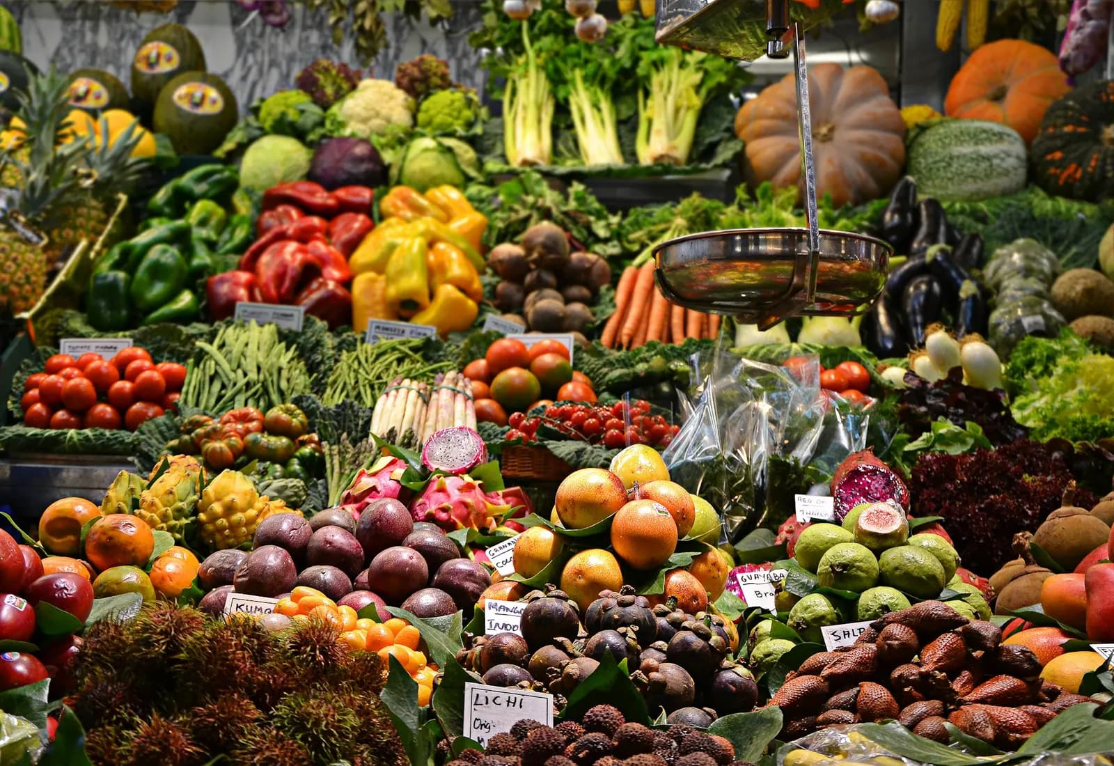 Puesto de mercado repleto de frutas y verduras frescas: zapallos, morrones, tomates, hojas verdes y cítricos