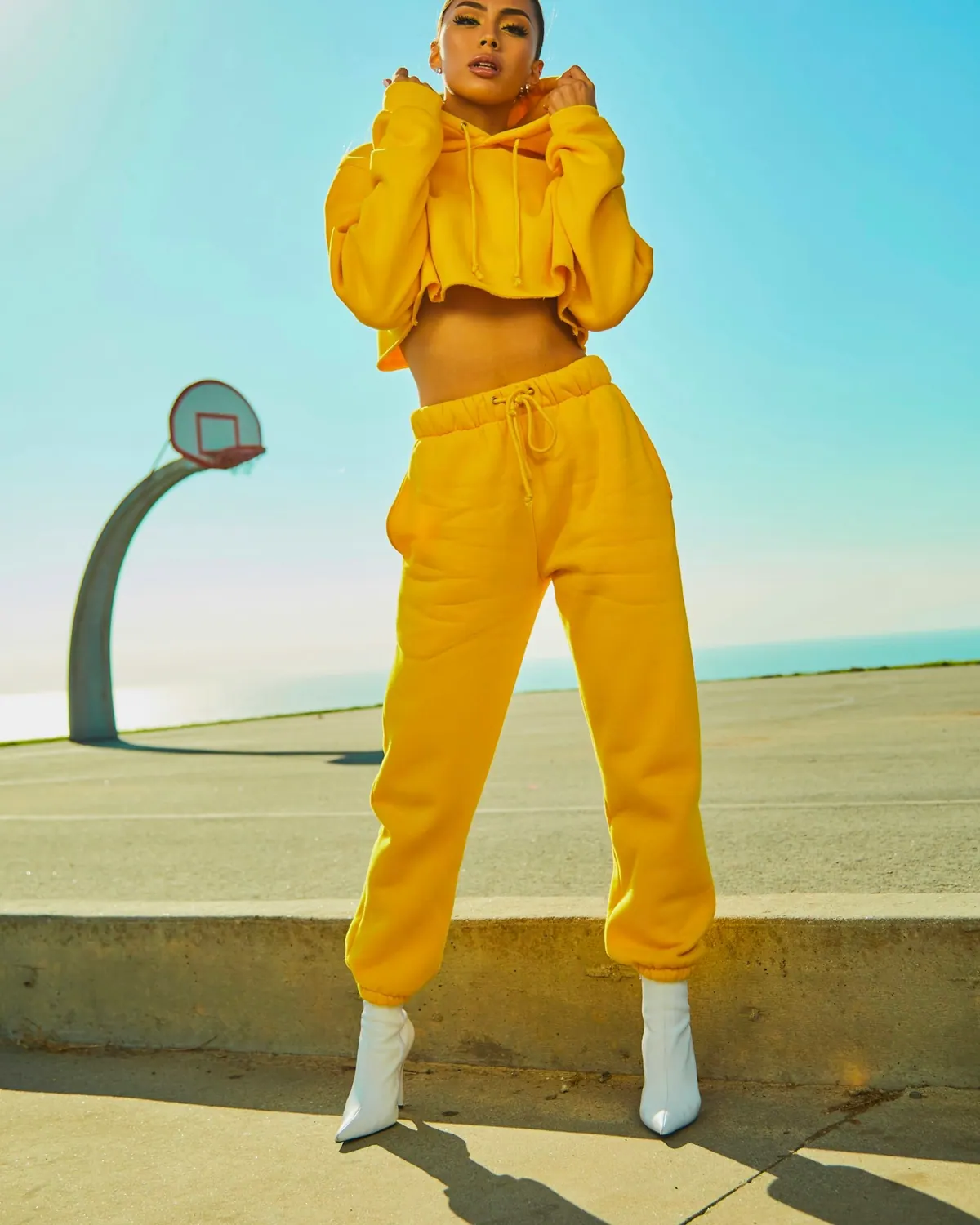 Look 01: mujer con buzo corto y jogger amarillos y botas blancas, en una cancha de básquet al aire libre