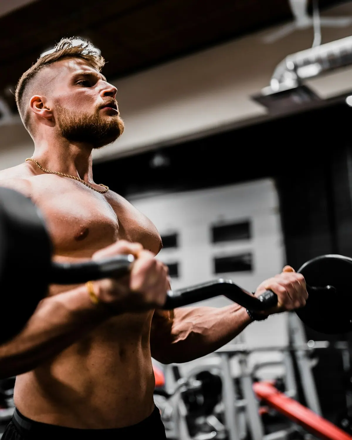 Atleta con barba haciendo curl de bíceps con barra en un gimnasio oscuro
