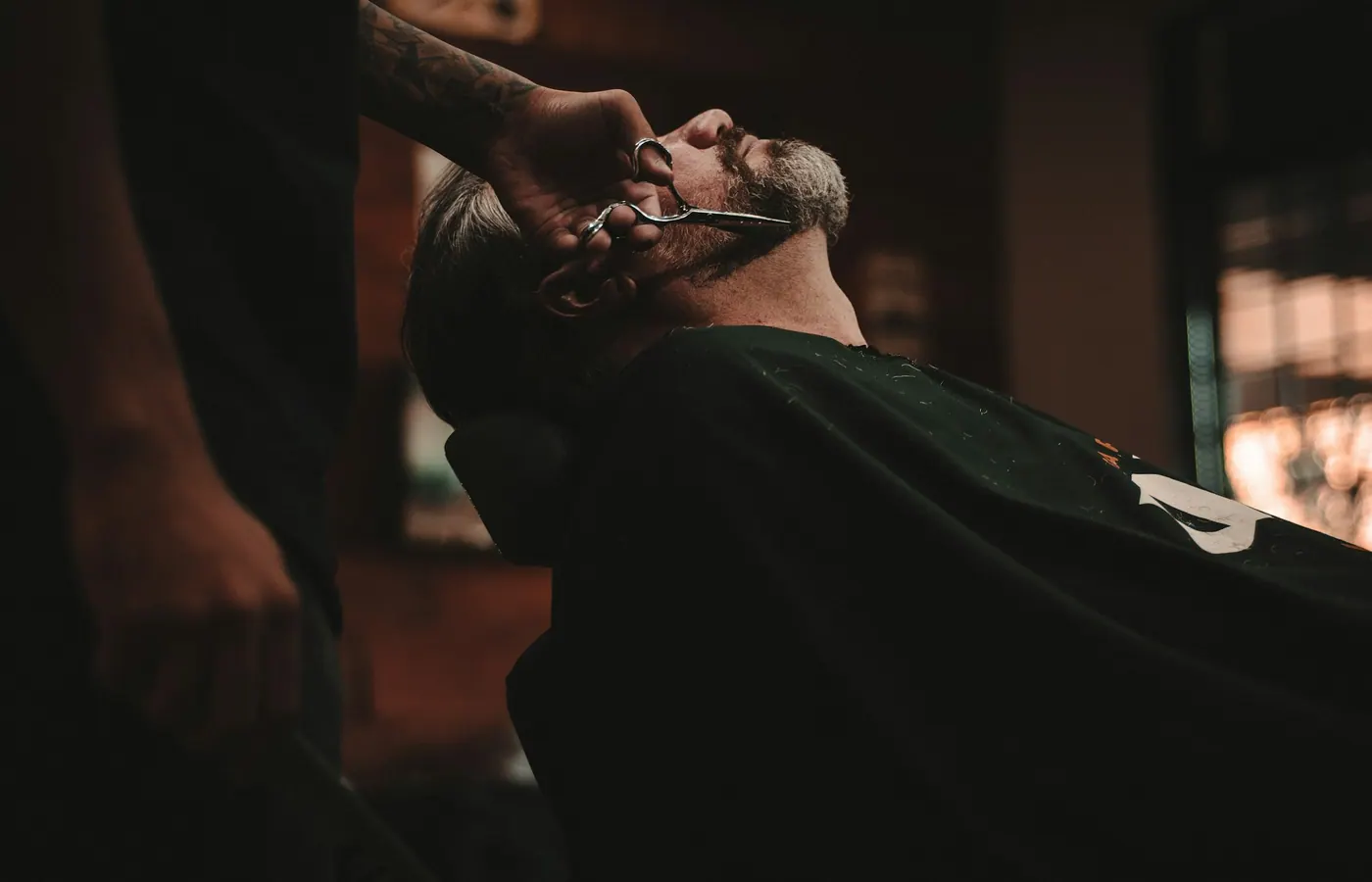 Barbero afeitando a navaja a un cliente reclinado en el sillón, en penumbra cálida
